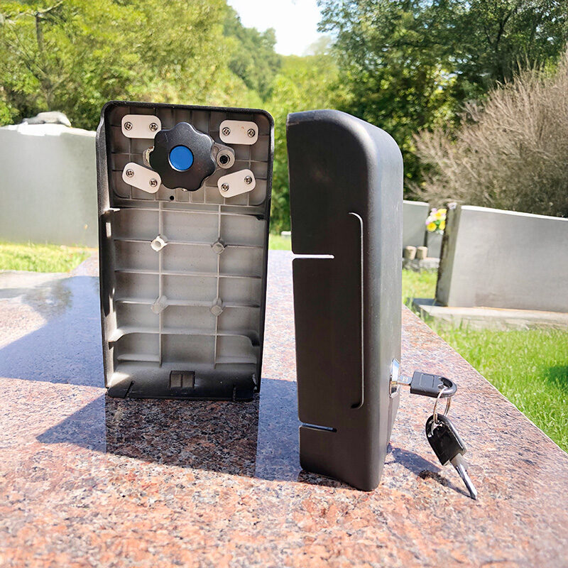 adjustable-security FlashBack memorial device shown open on a headstone, displaying the internal clamp system and exterior lock with keys inserted, ready for secure mounting.